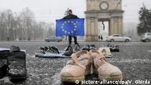 23.02.2019, Moldau, Chisinau: Ein Mann hält eine Flagge der Europäischen Union und steht hinter mehreren Schuhpaaren. Die Schuhe gehören Moldauern, die in anderen Ländern arbeiten. Viele Moldauer begründen die hohen Auswandererzahlen mit der Korruption und der schlechten Wirtschaftslage von Moldau. Foto: Vadim Ghirda/AP/dpa +++ dpa-Bildfunk +++ |