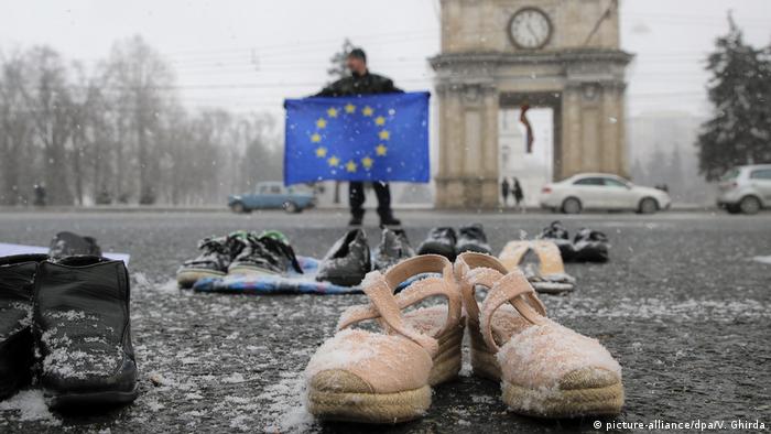 Trg u glavnom gradu Moldavije: Mladić drži zastavu EU a ispred njega obuća koja simbolizira mlade koji odlaze