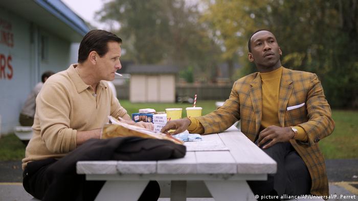 Film Green Book - Szene mit einem schwarzen und einem weißen Darsteller bei einer Picknick-Pause draußen an einem Holztisch (picture alliance/AP/Universal/P. Perret)