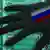 A hand with a Russian flag reaches out over a screen displaying computer code