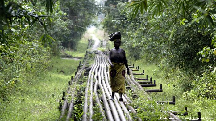 A woman walks along an oil pipeline near Shell's Utorogu flow station in Warri, Nigeria