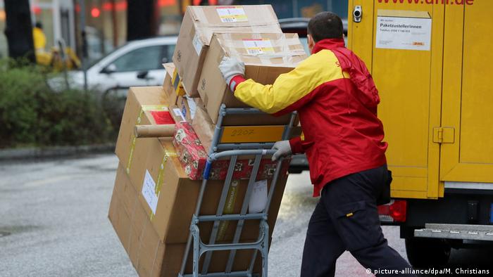 A courier from German postal service DHL delivering an assortment of big and small packages mounted on a push cart