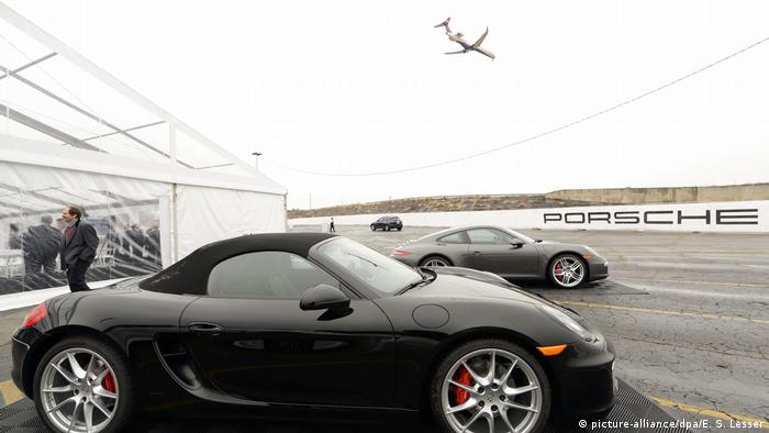 Two parked Porsches with a plane landing in the background