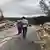 Duas pessoas caminham abraçadas numa estrada. Escombros são vistos de ambos os lados da rodovia