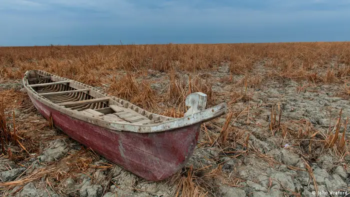 A traditional canoe-like boat sits on the dry and cracked marshland (photo: John Wreford)