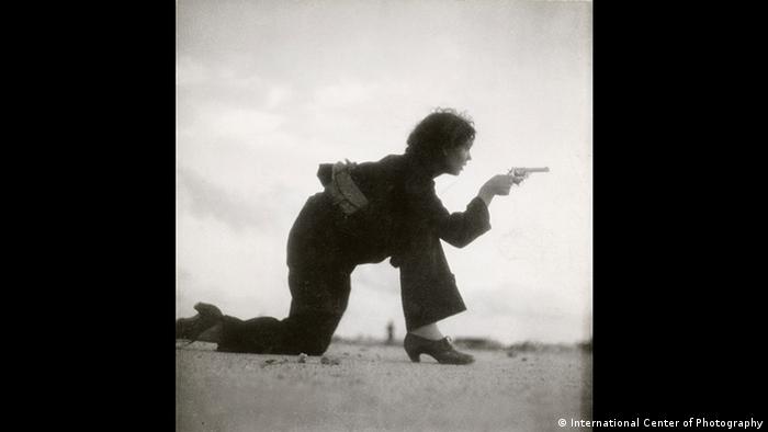 Eine Frau mit Revolver kniet am Strand (International Center of Photography)