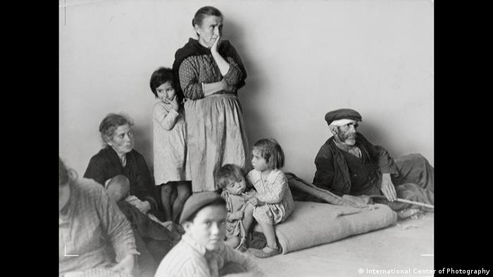 Eine Frau steht neben mehreren Kindern, neben ihr liegt ein alter Mann mit Kopfverband (International Center of Photography)