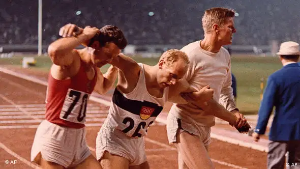 Willi Holdorf (Mitte) brach nach dem 1500m Lauf am 20. Oktober 1964, während der XVIII. Olympischen Spiele in Tokio, erschöpft zusammen. Mit diesem Lauf sicherte er sich die Goldmedaille