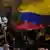 Foto simbólica de una persona con una flor blanca en la mano y la bandera de Colombia en el fondo.