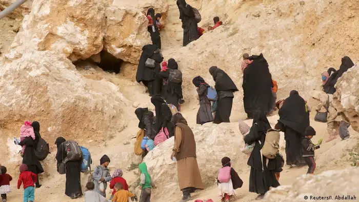 Surrendering families of IS militants walk up a rocky path