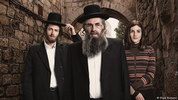 Two Orthodox Jews in hats and long beards, next to them a woman in a striped sweater (Ohad Romano)