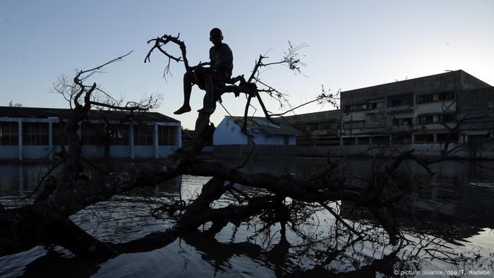 Un niño sentado en un árbol derribado frente a los edificios inundados tras el ciclón Idai. 