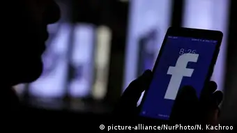 person holding smartphone displaying facebook app