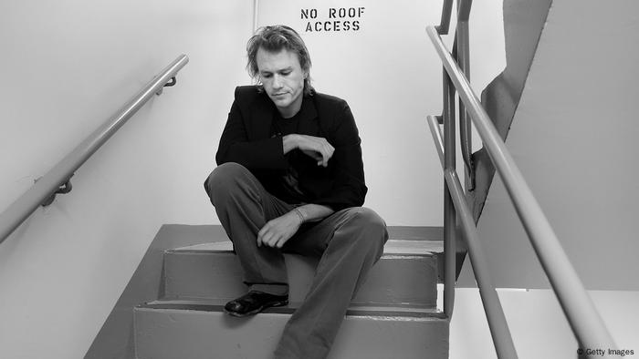 Black and white photo of actor Heath Ledger sitting on a staircase in 2008.