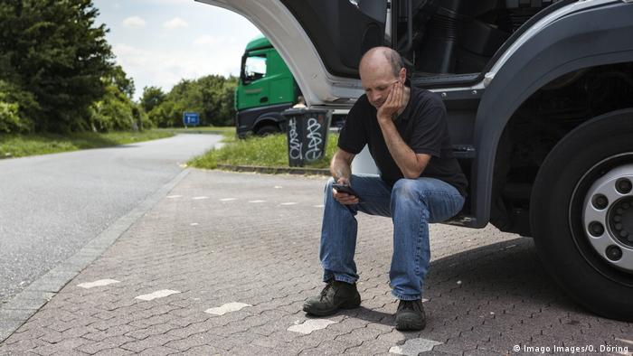 Ein Lkw-Fahrer sitzt während seiner Ruhezeit auf dem Trittbrett des Lastwagens