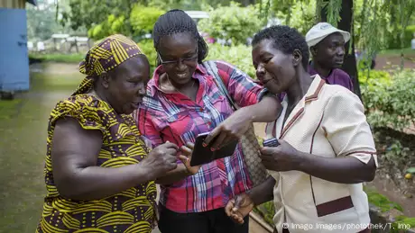 Three women are kooking at a smartphone, one holding another phone in her hand