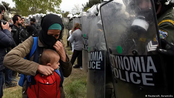 A refugee holds her child in front of Greek police in Diavata