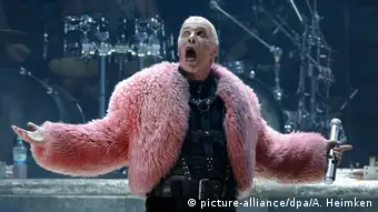 Rammstein singer Till Lindemann wears a pink coat and opens his mouth onstage