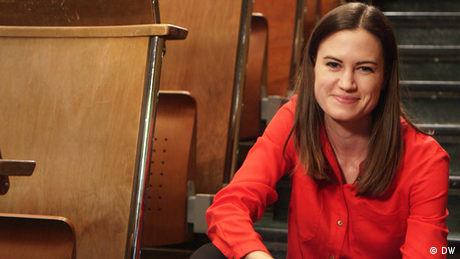 Rachel Stewart sits on stairs by desks in what appears to be a lecture hall and smiles
