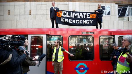 A man and a woman stand on top of a London train holding a sign that says climate emergency