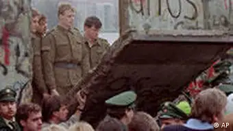 East German border guards look through a hole in the Berlin wall after demonstrators pulled down one segment of the wall at Brandenburg gate in this Nov. 11, 1989 file picture