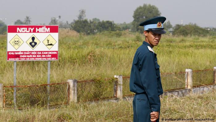 Ein vietnamesicher Soldat vor einem Warnschild, das vor dem betreten eines verseuchten Brachlandes warnt. 
