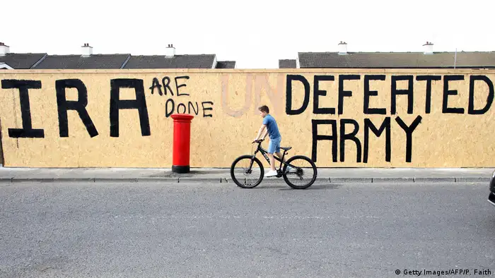 A pedestrian walks past graffiti that has been amended to read IRA are done. Defeated Army