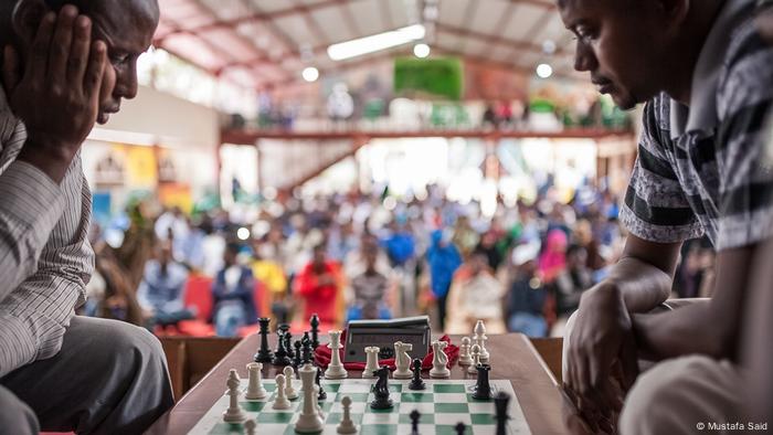 Check Mate, Everyday Africa: Zwei Schachspieler, über das Brett gebeugt, im Hintergrund Zuschauer (Mustafa Said)