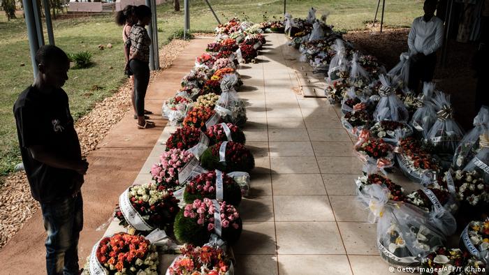 People stand by flowers laid on the mass grave