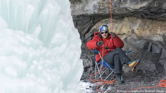Ice climber Will Gadd sits in a chair holding a belay rope next to a glacier