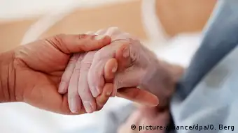 A hand of a younger person holds an older person's hand