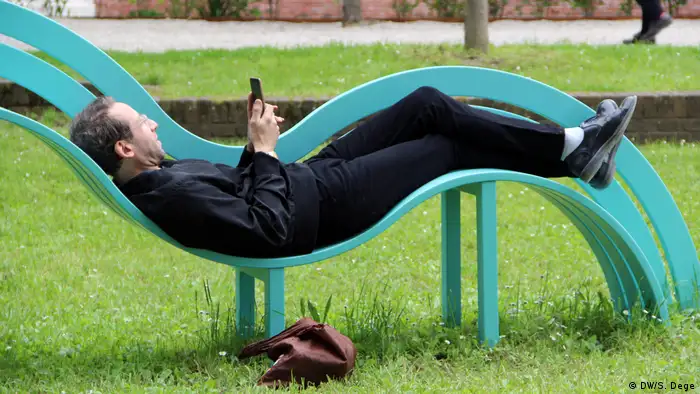 Ein Mann liegt in einer Bankskulptur und schaut in sein Handy (DW/S. Dege)