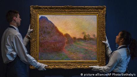 Two auction helpers hold up a Monet painting of haystavks (picture-alliance/AP Photo/Sotheby's)