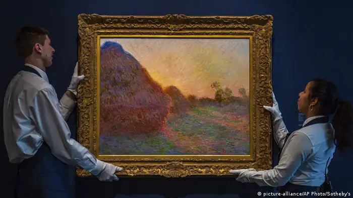 Two auction helpers hold up a Monet painting of haystavks (picture-alliance/AP Photo/Sotheby's)