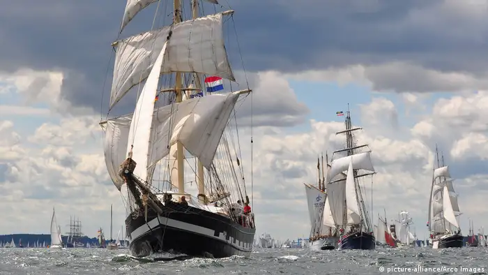 Three large sailing ships can be seen in the sea set against dramatic clouds in the sky