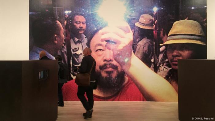 An exhibition photo of Ai Weiwei photographing himself surrounded by police officers.