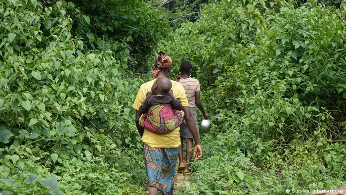A woman with a child on her back walks along a path through the forest