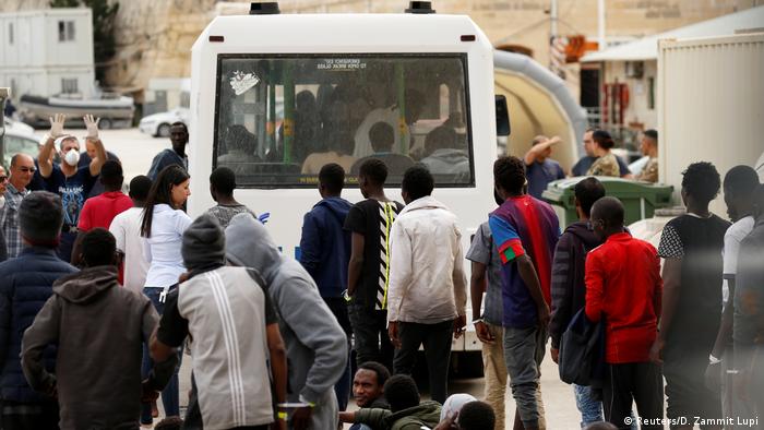 Migrants on shore, with a white ambulance in the background