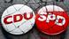 Anstecker der Volksparteien CDU und SPD auf brüchigem Grund Anstecker der Volksparteien CDU und SPD auf brüchigem Grund