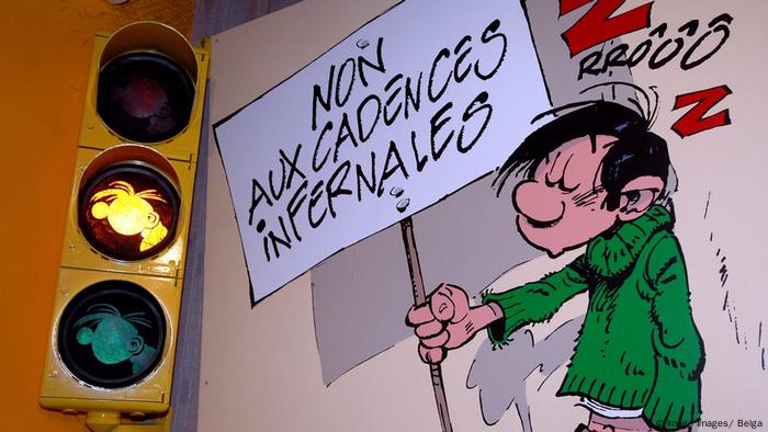 Gaston Lagaffe steht neben einer Ampel mit gelbem Licht und hält ein Plakat hoch (Imago Images/ Belga)