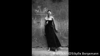 Ein Model steht in schwarzem Kleid vor einer bröckelnden Mauer
