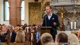 Un homme prononce un discours au pupitre d'une église, entouré d'auditeurs