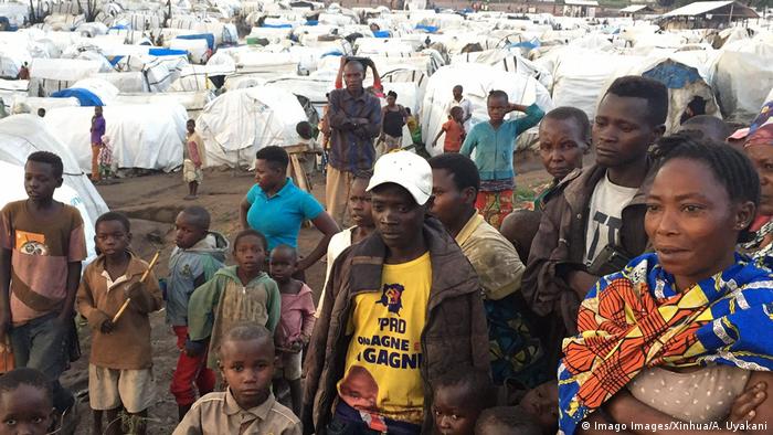 Men, women and children stand in front of an IDP camp
