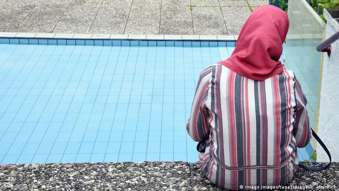 A Muslim woman in a headscarf sits by a pool in Berlin