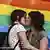 Two women kissing in front of rainbow banner