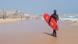 A surfer walking along the beach with a red board A surfer walking along the beach with a red board