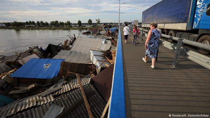 Жители Иркутской области смотрят с автомобильного моста на руины домов, разрушенных наводнением. 