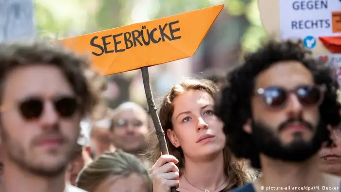 Protester holding up ship-shaped placard (picture-alliance/dpa/M. Becker)