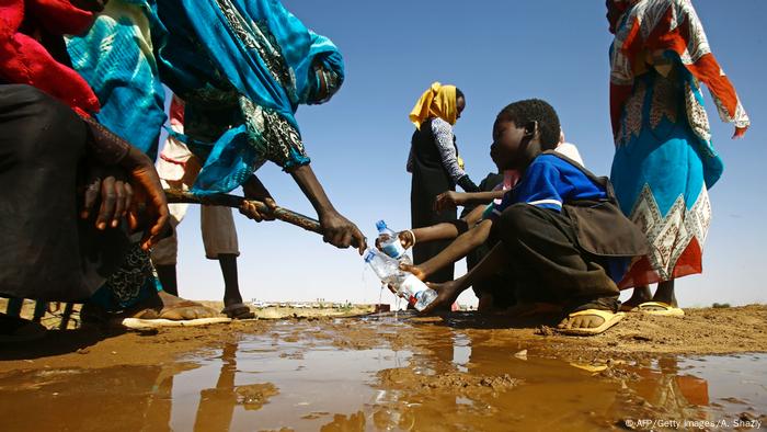 A Sudanese woman fills water bottles held by a young boy about 60 kilometres north of El-Fasher, the capital of the North Darfur state