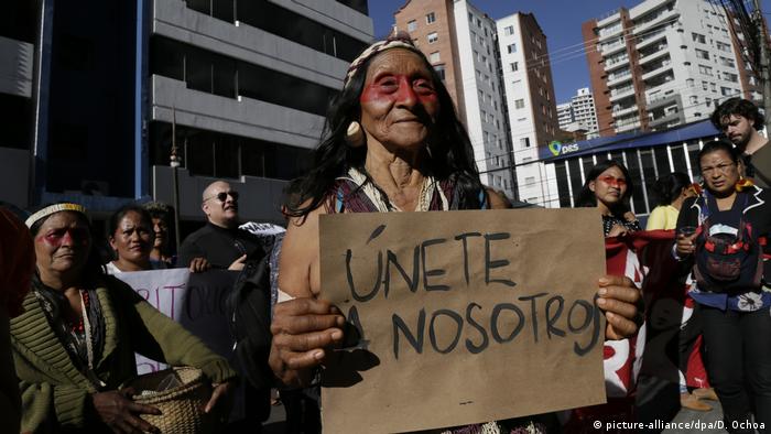 Eine Angehörige des indigenen Volkes der Waorani hält bei einer Demonstration in Quito ein Plakat in den Händen. Auf Spanisch steht darauf Schließt euch uns an! geschrieben.